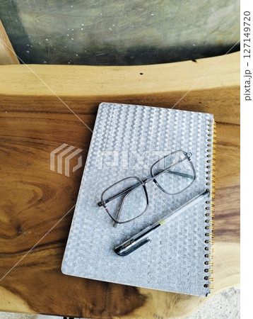 Open notepad with pen and glasses on wooden table. A Blank Sheet Of Notebook With The Items Of A Businessman. Ideal for branding and note-taking app presentations. Close up Open notepad with pen and glasses on wooden table. A Blank Sheet Of Notebook With The Items Of A Businessman. Ideal for branding and note-taking app presentations. Close up 127149720