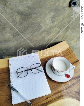 Notebook, pen, glasses and a cup of milk on the wooden table 127149948