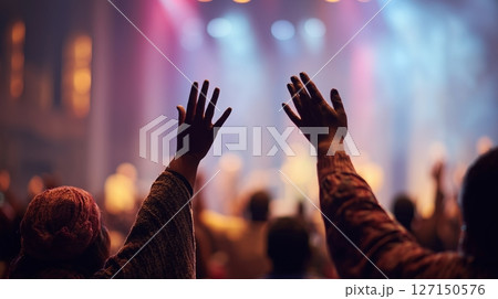 Devout christians worship with hands raised in prayer during an energetic service in a vibrant church environment 127150576