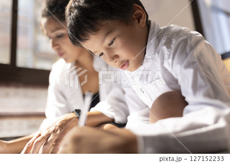 Focused asian boy drawing next to his mother at home 127152233