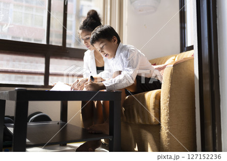 Mother helping son with homework in living room 127152236