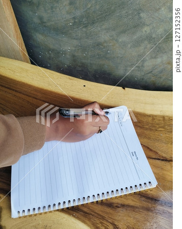 Hand Writing Notes in Journal on Light Wood Table Planning Concept Hand Writing Notes in Journal on Light Wood Table Planning Concept 127152356