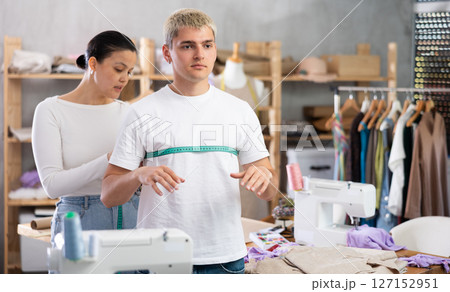 Young Asian tailoress measuring male client in sewing workshop 127152951