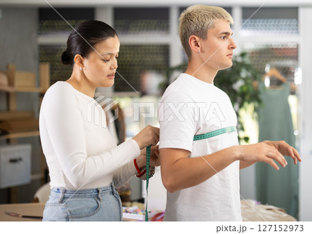 Professional young female fashion designer taking measurements of male client for sewing clothes in tailor shop 127152973