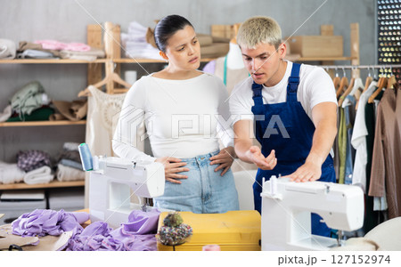 Professional young repairman master repairing sewing machine in sewing workshop, excited asian woman seamstress asking questions 127152974