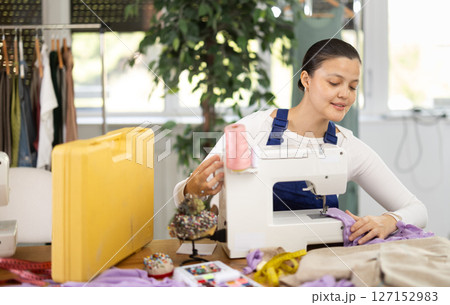 Repairwoman master is collecting and testing sewing machine after repairing sitting at table in sewing workshop 127152983