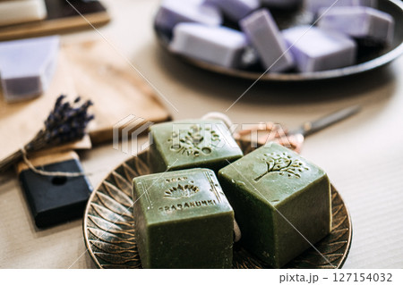 Green stamped soap bars rest on a plate beside lavender soaps and artisan tools. Artisanal process, indie skincare, microbrand identity, handmade beauty products 127154032