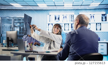 Senior man patient meeting with his doctor to discuss results in an office, using advanced tools to provide diagnostic report. Medic doing x ray scans interpretation, professional approach. Camera A. Senior man patient meeting with his doctor to discuss results in an office, using advanced tools to provide diagnostic report. Medic doing x ray scans interpretation, professional approach. Camera A. 127155613