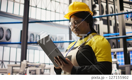 Solar panels plant expert uses tablet to oversee systems, ensuring machinery operates at optimal efficiency. Photovoltaics plant employee uses device software to maintain operations, camera A close up Solar panels plant expert uses tablet to oversee systems, ensuring machinery operates at optimal efficiency. Photovoltaics plant employee uses device software to maintain operations, camera A close up 127155902