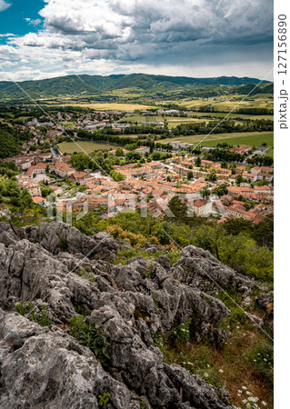 Picturesque View Of Vipava From Castle Ruins: Red-Tiled Rooftops And Church Tower Nestled In Green Valley With Blooming Flowers In Foreground And Rolling Fields In Background, Slovenia 127156890
