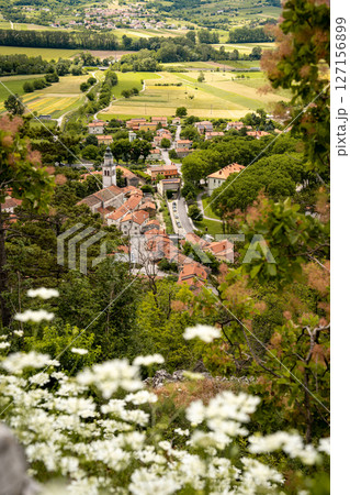 Picturesque View Of Vipava From Castle Ruins: Red-Tiled Rooftops And Church Tower Nestled In Green Valley With Blooming Flowers In Foreground And Rolling Fields In Background, Slovenia Picturesque View Of Vipava From Castle Ruins: Red-Tiled Rooftops And Church Tower Nestled In Green Valley With Blooming Flowers In Foreground And Rolling Fields In Background, Slovenia 127156899