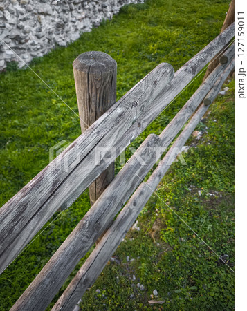 Weathered wooden fence bordering verdant grass, rustic landscape detail in autumn countryside near aosta, italy 127159011