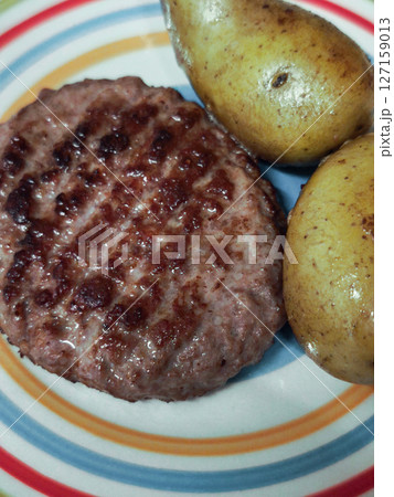 Grilled beef patty resting on striped plate, golden boiled potatoes representing rustic aosta valley cuisine 127159013