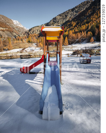 Snow covered playground slide nestled amid golden autumn landscape of aosta valley mountain scenery Frazionne Lillaz Snow covered playground slide nestled amid golden autumn landscape of aosta valley mountain scenery Frazionne Lillaz 127159019