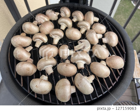 Roasted grilled mushrooms with garlic and herbs and served on a wooden board in kamado style grill 127159063