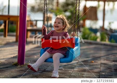 Portrait of a adorable little girl laughing when playing a swing Portrait of a adorable little girl laughing when playing a swing 127159381