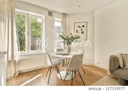 A stylish dining area featuring a round table surrounded by elegant chairs, large windows letting in natural light, and a touch of greenery. A stylish dining area featuring a round table surrounded by elegant chairs, large windows letting in natural light, and a touch of greenery. 127159577