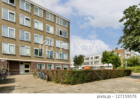 A contemporary building featuring large windows, surrounded by trees and manicured shrubs, with bicycles parked in front, showcasing urban living. A contemporary building featuring large windows, surrounded by trees and manicured shrubs, with bicycles parked in front, showcasing urban living. 127159578