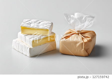 Soft cheese wedges resting on white surface with wrapped option nearby. Minimalist presentation highlights culinary appeal. Concept of food industry, catering, gourmet markets 127159742