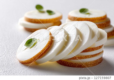 Mozzarella slices are artistically layered on a clean white surface, highlighting their smooth textures and delicate appearance. Concept of culinary arts, food photography, gourmet cheese 127159807