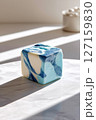 Marbled blue and white cheese cube placed centrally on clean white background. Soft natural light creates gentle shadows in modern minimalist setting 127159830