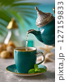 Ceremonial pour of Moroccan mint tea from silver teapot creates emerald waterfall effect. Bright, tropical background enhances vibrant ambiance 127159833
