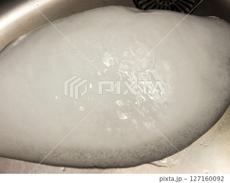 A piece of ice in a metal sink. 127160092