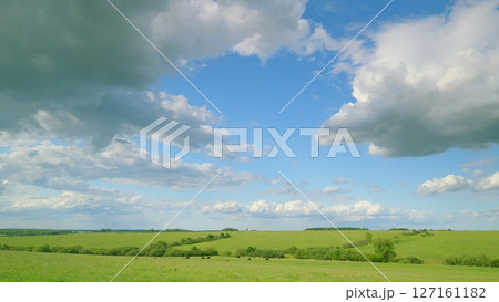 A serene and peaceful landscape featuring a bright blue sky and lush green fields all around 127161182