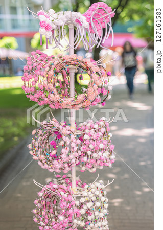 Colorful flower headbands with mini roses in shades of pink and white displayed on street market stand. Traditional cultural Rose festival. Concept of romantic accessory, festive charm Colorful flower headbands with mini roses in shades of pink and white displayed on street market stand. Traditional cultural Rose festival. Concept of romantic accessory, festive charm 127161583