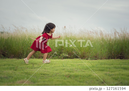 happy toddle girl in red dress running on grass field 127161594