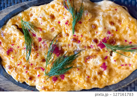 Cheesy baked potato dish in a cast iron skillet garnished with dill sprigs and seasoning. Close-up Cheesy baked potato dish in a cast iron skillet garnished with dill sprigs and seasoning. Close-up 127161783