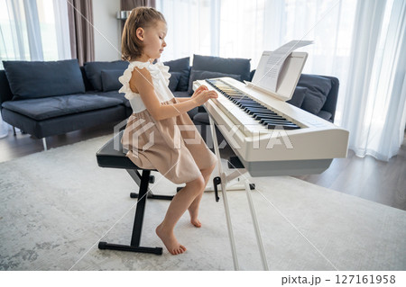 Little girl playing piano at home in the living room. Childhood creativity and musical development in cozy family environment 127161958