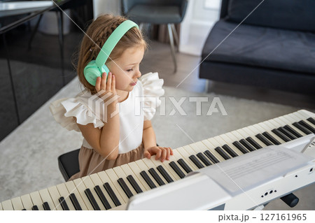 Little girl practicing piano with wireless headphones at home. Early childhood development through modern and focused music education. Little girl practicing piano with wireless headphones at home. Early childhood development through modern and focused music education. 127161965