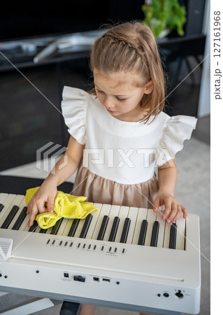 Little girl carefully cleaning her piano at home in the living room. Early childhood education through music includes care, responsibility and respect for the instrument. 127161968