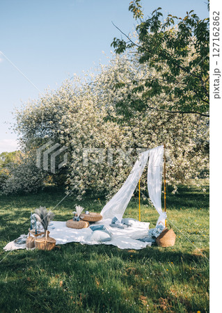 Cozy outdoor picnic setup under blooming trees in a serene park on a sunny day 127162862