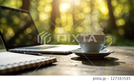 Outdoor workspace with laptop, notebook, and steaming coffee cup 127163585