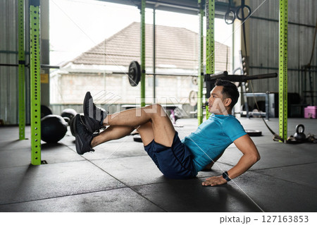 Fitness Core Exercise. Man performing a bicycle crunch in a gym. Fitness Core Exercise. Man performing a bicycle crunch in a gym. 127163853