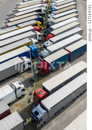 Aerial view of a large truck parking lot at a logistics hub, with multiple commercial semi trucks parked in organized rows Aerial view of a large truck parking lot at a logistics hub, with multiple commercial semi trucks parked in organized rows 127164191