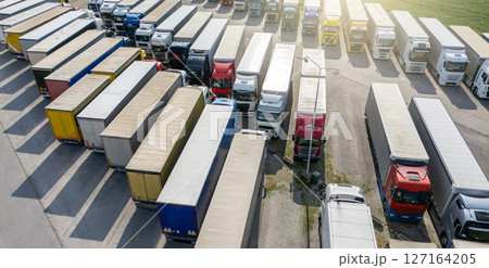 Aerial view of a large truck parking lot at a logistics hub, with multiple commercial semi trucks parked in organized rows. 127164205