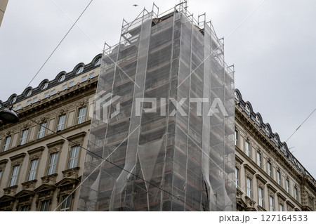 Historic building wrapped in scaffolding mesh during restoration, concept of urban renovation Historic building wrapped in scaffolding mesh during restoration, concept of urban renovation 127164533
