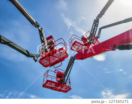 Workers operating lift equipment under clear blue sky during outdoor construction activity near urban area 127165271