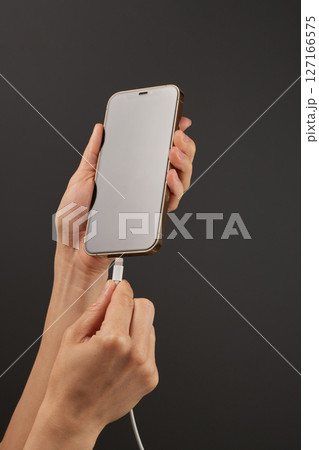 female hand plugging charger cord into smartphone to charge battery isolated on black background, Wired charging 127166575