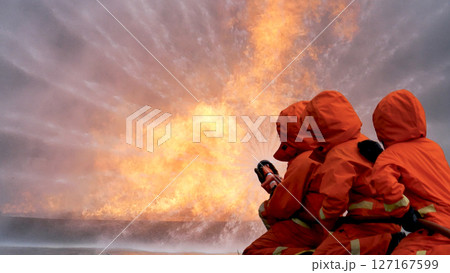 Firefighter Rescue team training in fire fighting extinguisher. Teamwork Firefighter fighting with flame using fire hose chemical water foam spray engine. Fireman teams wear hard hat safety uniform 127167599