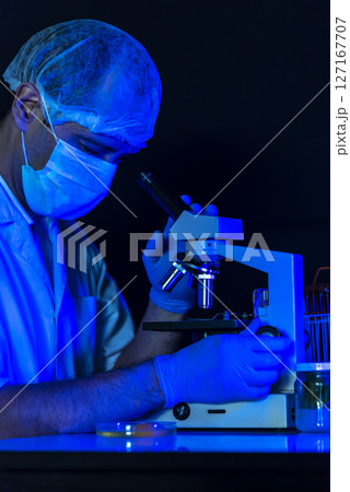 Vertical Scientist men in lab look at science microscope medical test researching biology chemistry with blue light black background. Male technician laboratory analyze Chemistry Medical research Vertical Scientist men in lab look at science microscope medical test researching biology chemistry with blue light black background. Male technician laboratory analyze Chemistry Medical research 127167707
