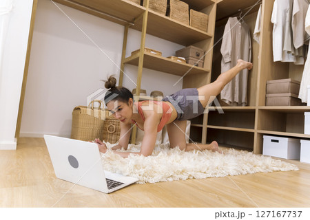 Young Sport Women look at laptop online trainer home fitness workout exercise in living room. Woman using laptop on floor in sportswear arms stretching body weight traning. Healthy lifestyle concept 127167737