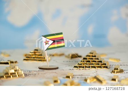 Miniature Zimbabwe flag stands amidst numerous precious shiny gold bars on a blurred world map, representing the nation's economic wealth and financial potential 127168728