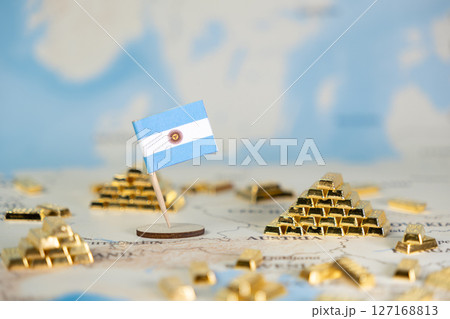 Argentinian flag and gold bar piles on a world map symbolize national wealth, economic stability, global finance, and commodity trade with copy space 127168813