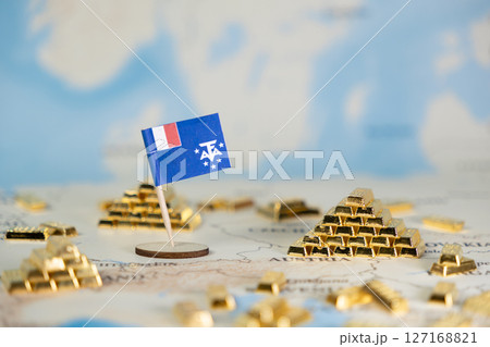 Miniature flag of French Southern and Antarctic Lands on a global map with numerous gold bars, symbolizing national resource wealth and economic strategic importance 127168821