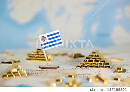 Miniature Uruguay flag stands proudly surrounded by golden bars on a global map, signifying national economic power, trade, and wealth accumulation, featuring ample copy space Miniature Uruguay flag stands proudly surrounded by golden bars on a global map, signifying national economic power, trade, and wealth accumulation, featuring ample copy space 127168892