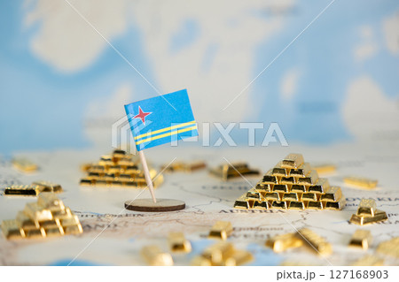 Aruba flag standing on a world map surrounded by golden bar piles, symbolizing international economy, investment, and national wealth for global finance 127168903